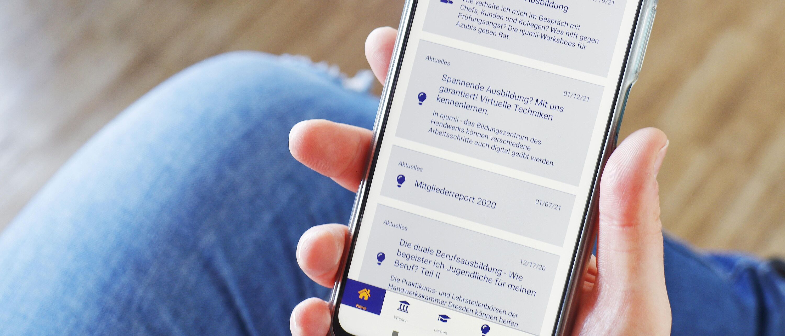 Eine Person hält ein Handy mit der geöffneten App \"Ausbilderwissen\" in der Hand.