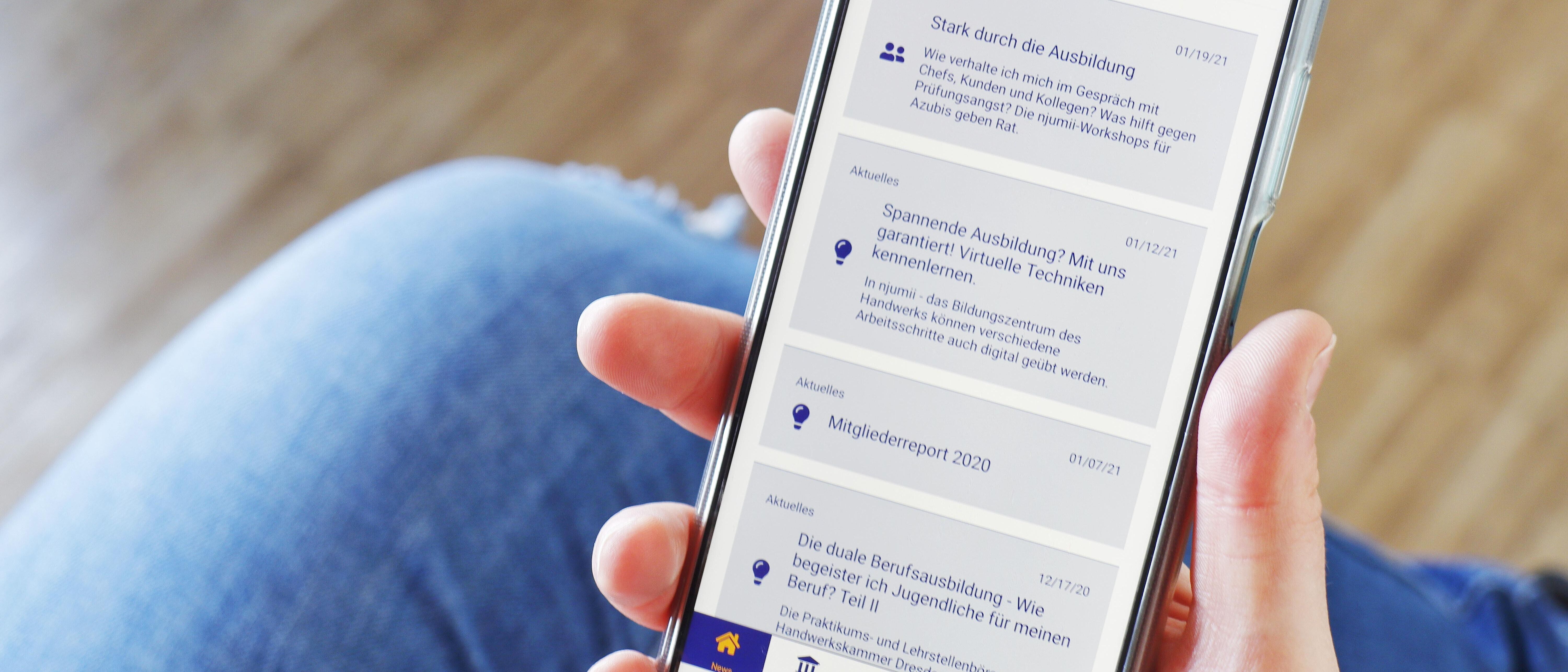 Eine Person hält ein Handy mit der geöffneten App \"Ausbilderwissen\" in der Hand.