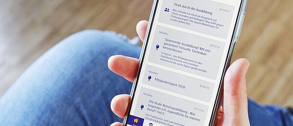 App \"Ausbilderwissen\" Eine Person hält ein Handy mit der geöffneten App \"Ausbilderwissen\" in der Hand.